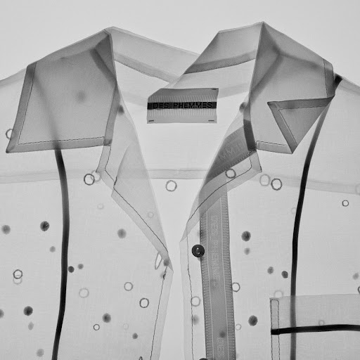 Sheer button-down shirt with polka dot-like accents and a collar, displaying a translucent texture and a clothing label, against white.