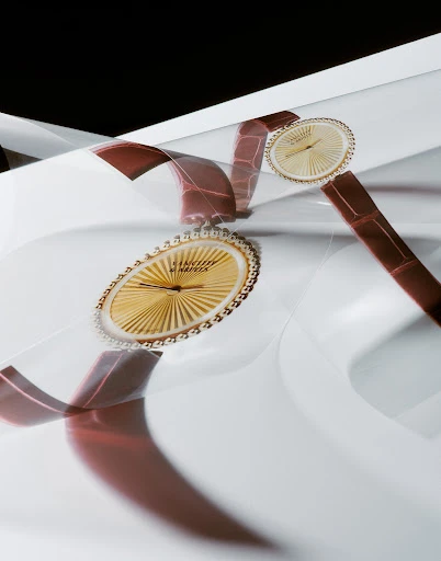Close-up studio shot of two golden wristwatches with brown leather straps on a white, reflective surface against a black background.