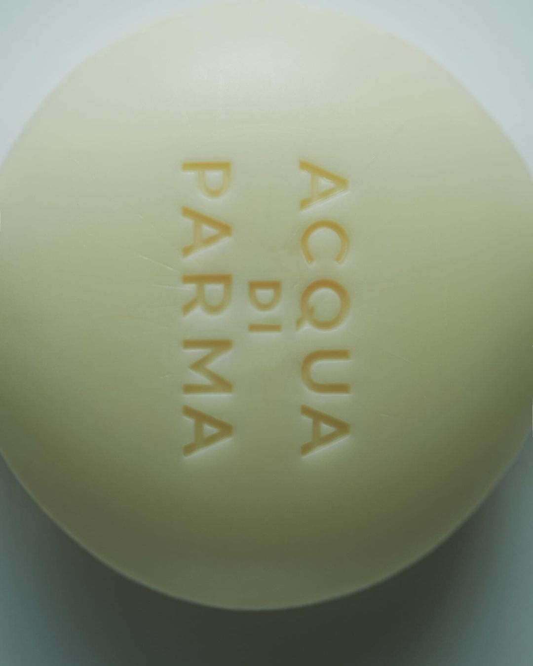 Close-up of a single bar of pale yellow soap with 'ACQUA DI PARMA' embossed on the surface, product shot on a neutral background.