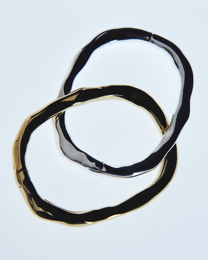Overlapping gold and silver bangles create an abstract composition, showcasing the metallic jewelry on a bright white background.