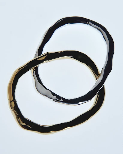Overlapping gold and silver bangles create an abstract composition, showcasing the metallic jewelry on a bright white background.