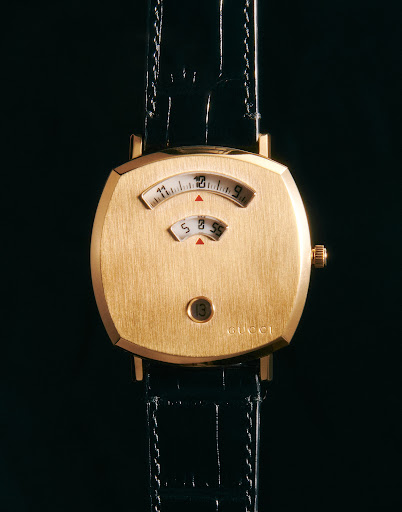 Close-up of a gold Gucci jump hour watch with a black leather strap, showcasing its unique time display and luxury design.