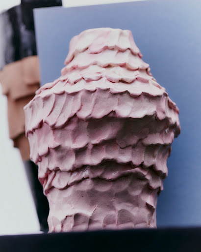 Abstract art sculpture with a tiered design, featuring pink and cream hues, set against a blue background. Contemporary art form.