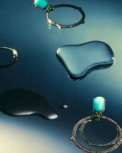 Close-up studio shot of turquoise and gold hoop earrings, with water droplets creating a reflective surface.