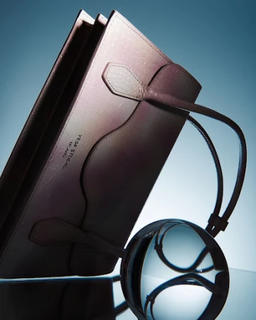 Close-up studio shot of a pink leather-bound folio with a clear crystal ball creating optical distortions and reflections on a glossy surface.
