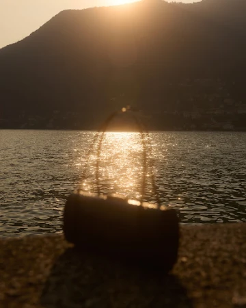 Silhouette of a handbag placed on a stone wall overlooking a lake at sunset, photographed by Sara Zanoni.