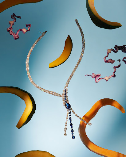 Elegant diamond and blue sapphire necklace with cantaloupe and artistic purple cabbage on a light blue backdrop for a vibrant, abstract feel.