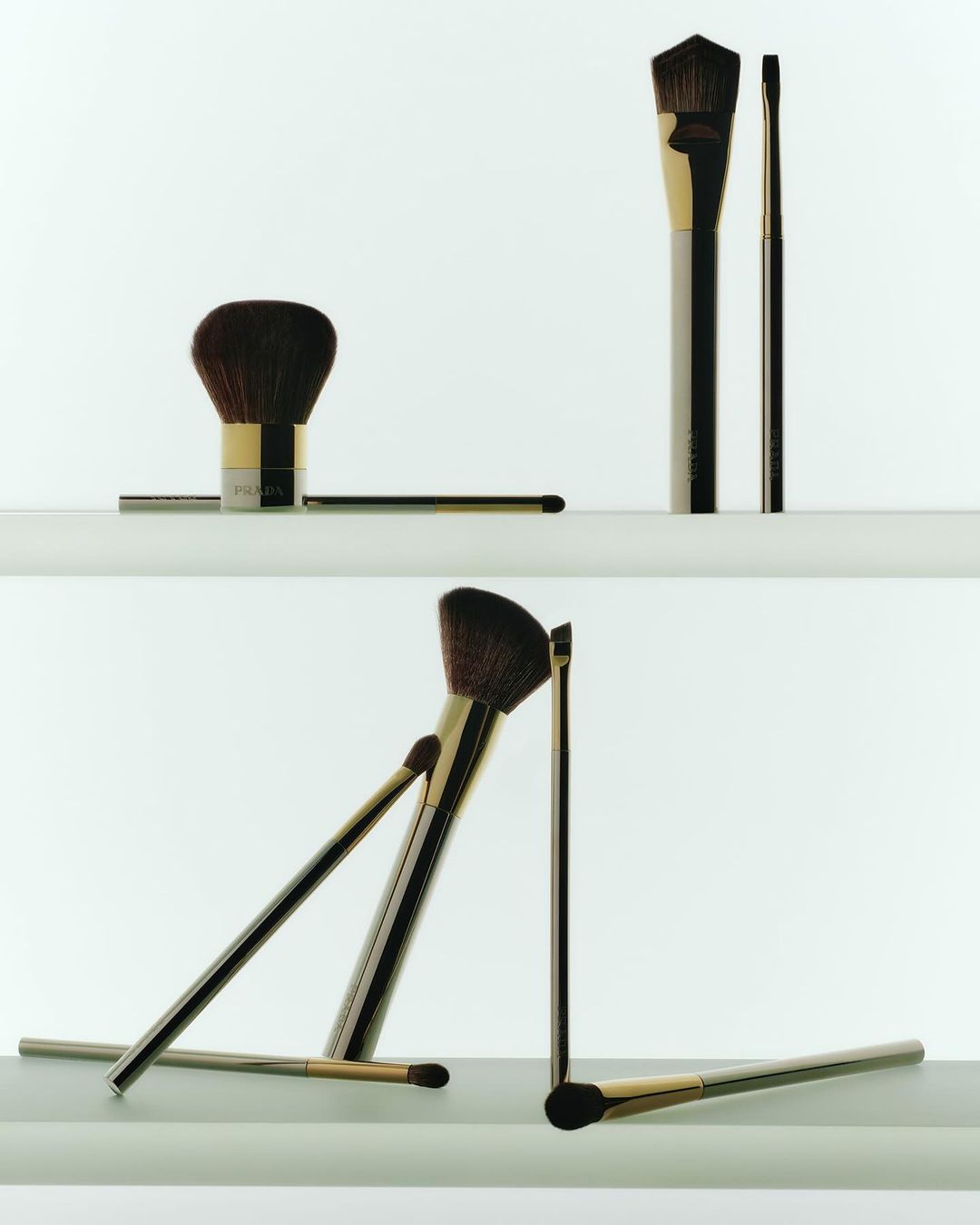 Still-life product shot featuring a set of golden-handled makeup brushes arranged in a visually balanced composition on white shelves.