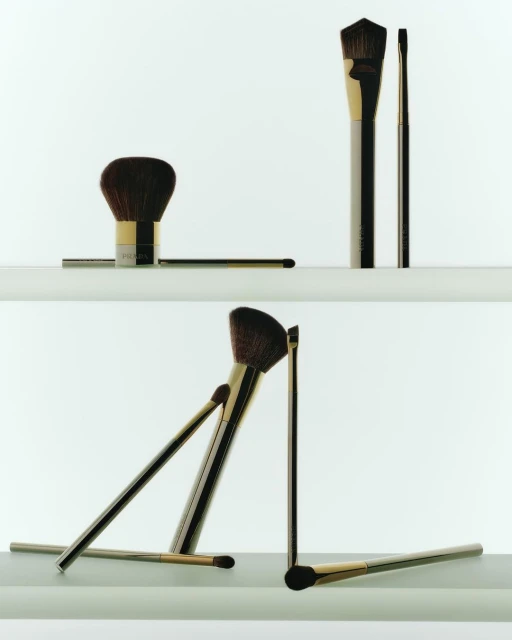 Still-life product shot featuring a set of golden-handled makeup brushes arranged in a visually balanced composition on white shelves.