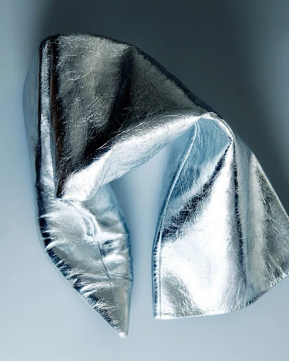 Close-up of a shiny silver metallic fabric draped and folded with a reflective surface, capturing light and shadow.