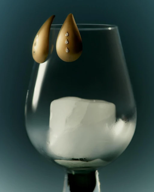 Elegant gold drop earrings with diamonds displayed inside a clear glass goblet with candle, creating a sophisticated jewelry still life.