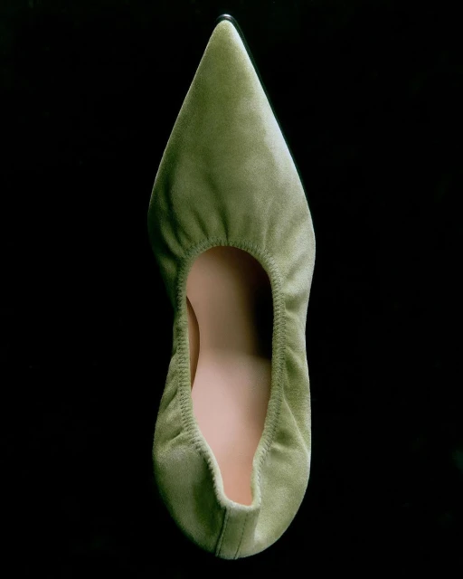 Overhead shot of a light green velvet ballet flat shoe with a pointed toe against a dark background in a studio setting. Minimalist footwear.