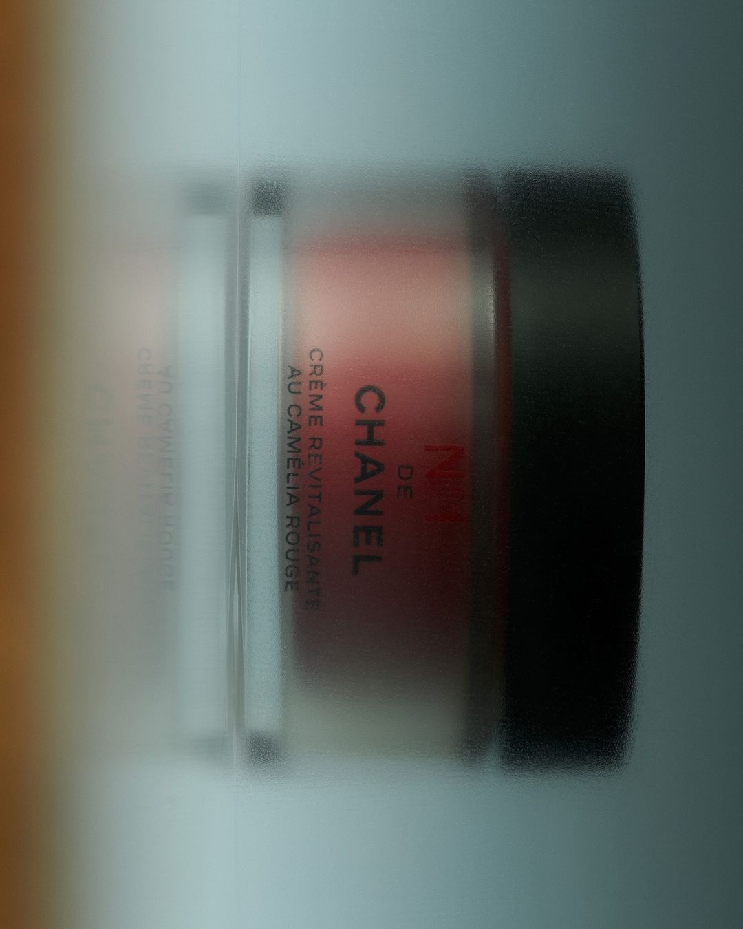 Cosmetic product in container with 'Chanel' branding. The container features a dark lid, clear sides, and creme filling.