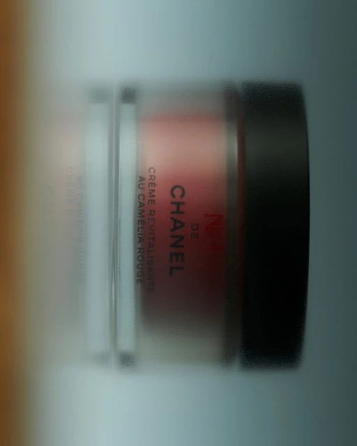 Cosmetic product in container with 'Chanel' branding. The container features a dark lid, clear sides, and creme filling.