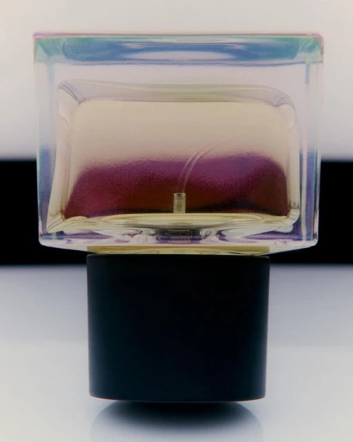 Close-up studio shot of a perfume bottle with a rectangular transparent glass body and a cylindrical black base on a reflective surface.