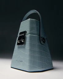 Light blue embossed leather handbag with a metal latch and top handle on a grey studio gradient background