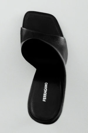 Top-down view of a black leather Ferragamo slide sandal on a minimal grey studio background