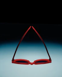 Red sunglasses inverted on a blue to black gradient studio background with temples meeting at top