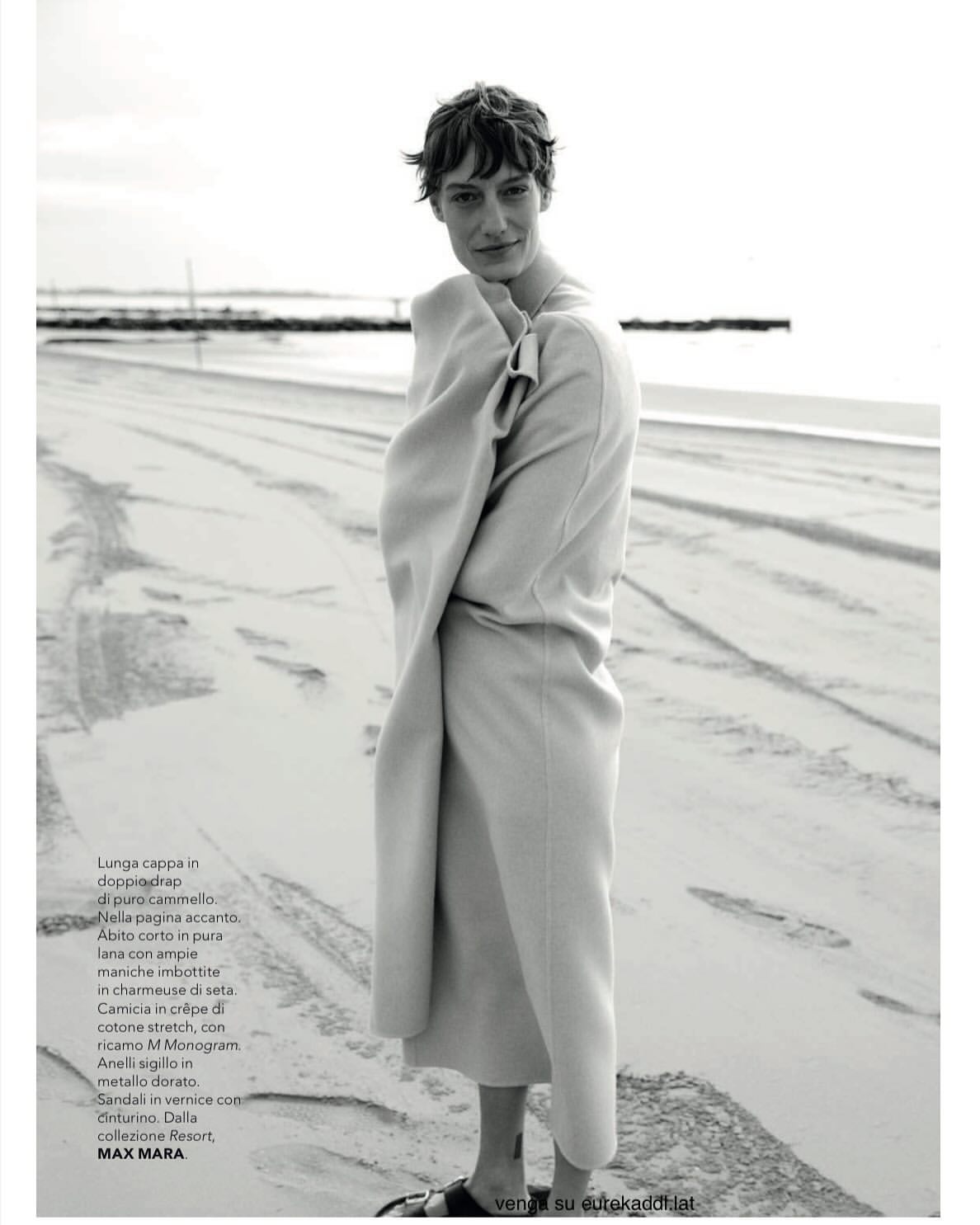 Model wrapped in a long coat standing on a sandy beach in a monochrome fashion editorial photograph by Stefano Galuzzi.