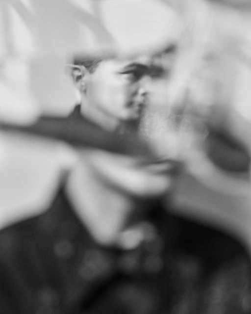 Monochromatic portrait of a blurry man with dark hair and clothing, creating an artistic and abstracted visual effect.