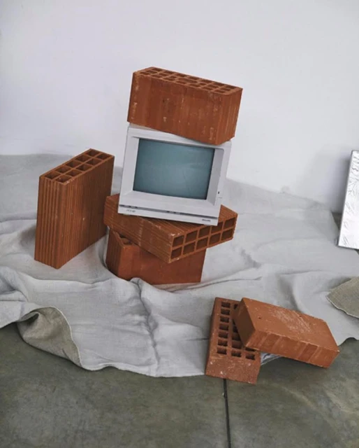 Still life of an old television monitor stacked on red bricks over a wrinkled white sheet against a white background in a studio.