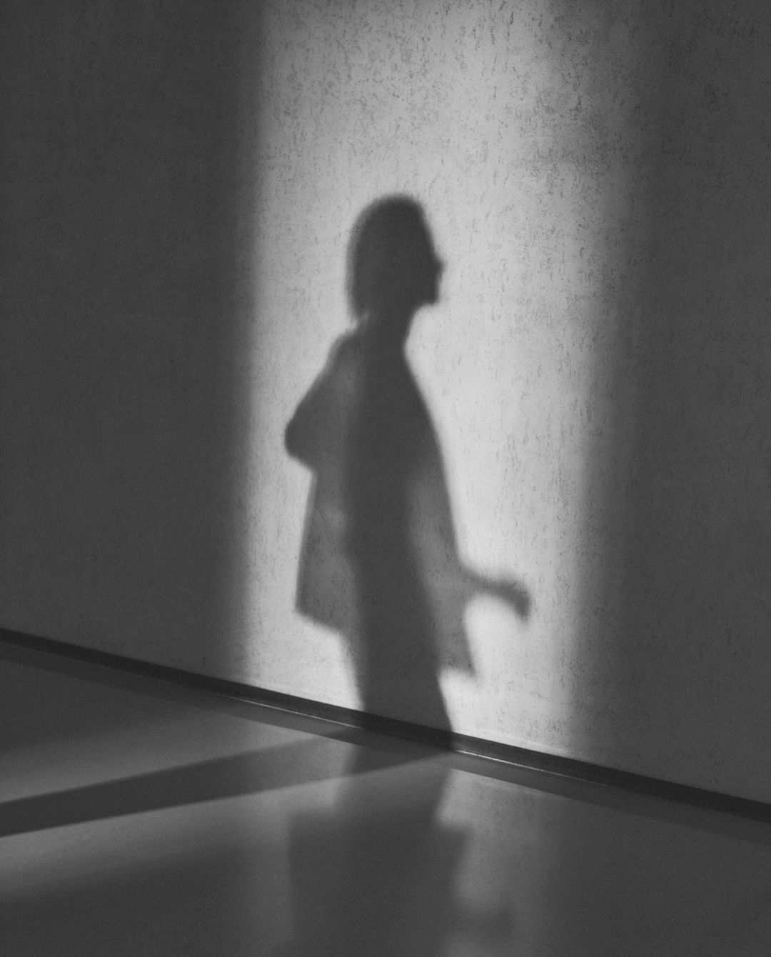 Monochrome image of a human shadow cast on a concrete wall next to a polished floor, creating a minimalist, high-contrast art piece.