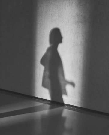 Monochrome image of a human shadow cast on a concrete wall next to a polished floor, creating a minimalist, high-contrast art piece.