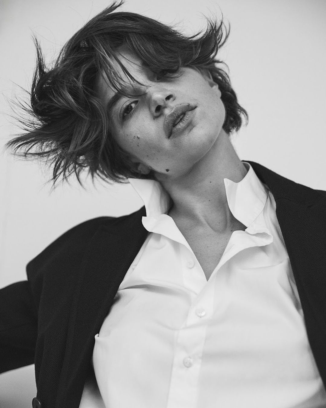 Monochrome portrait of a woman with short dark hair wearing a white collared shirt and dark blazer against a light background.