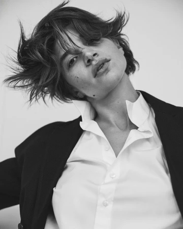 Monochrome portrait of a woman with short dark hair wearing a white collared shirt and dark blazer against a light background.