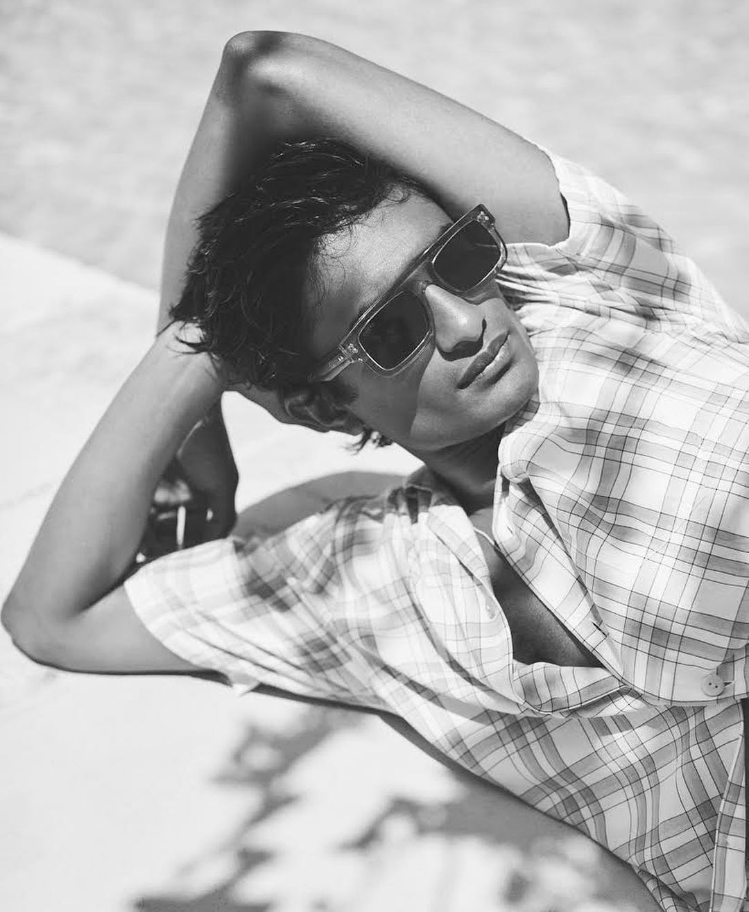 Portrait of a man lying down in direct sunlight wearing sunglasses and a patterned shirt, showcasing a relaxed and stylish outdoor scene.