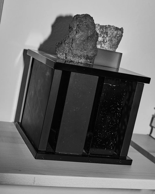 Still life shot of mineral rocks on a black rectangular display case against a light background in a monochrome photograph.