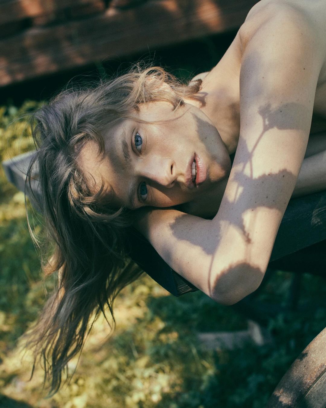 Portrait of a person resting chin on arms outdoors with dappled leaf shadows across their face and shoulder.