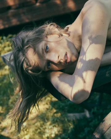 Portrait of a person resting chin on arms outdoors with dappled leaf shadows across their face and shoulder.