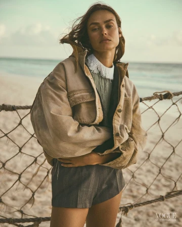 Model standing on a sandy beach wearing a beige jacket and grey shorts, photographed by Stefano Galuzzi.