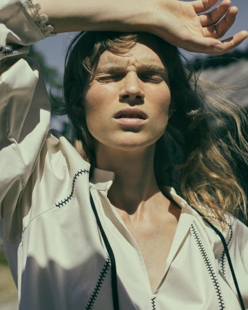 Model with eyes closed holding arm over forehead wearing cream tunic with black stitching by Stefano Galuzzi