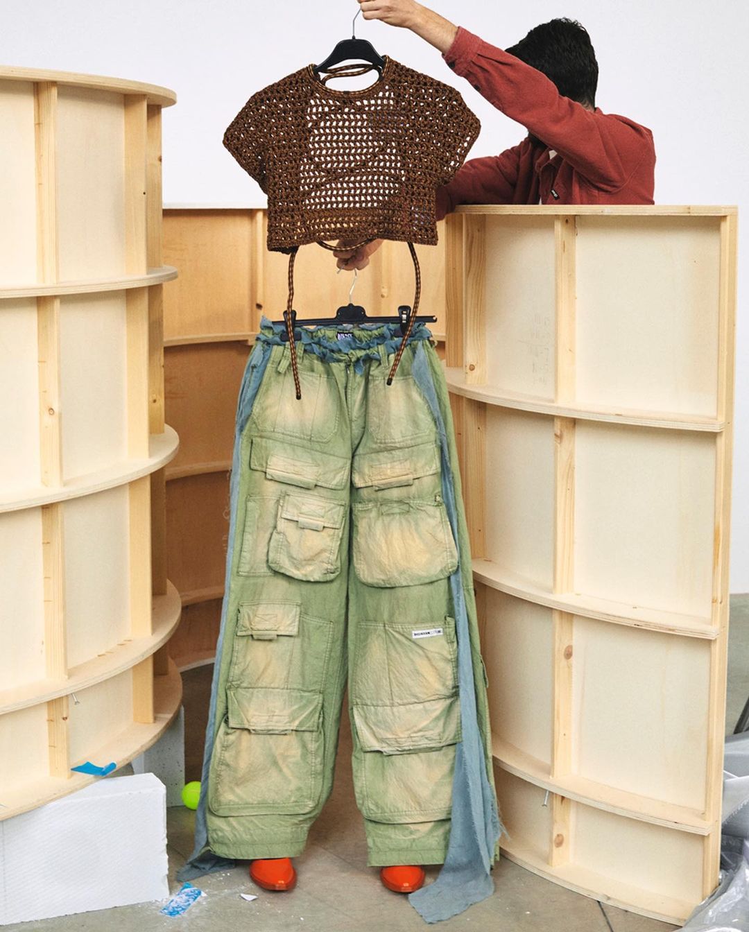 Fashionable brown crocheted crop top paired with wide-leg green cargo pants held up by a human in a light studio setting.