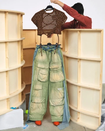Fashionable brown crocheted crop top paired with wide-leg green cargo pants held up by a human in a light studio setting.