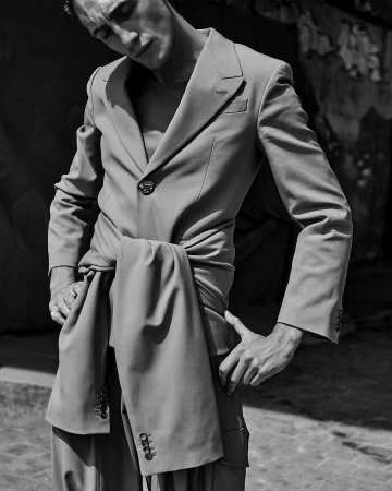 Monochrome portrait of a male model wearing a tailored suit jacket with sleeves tied around his waist.