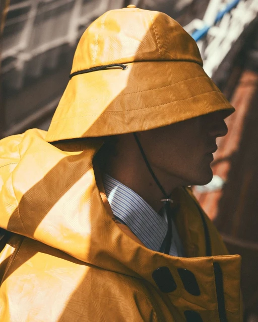 Profile shot of a person wearing a yellow fisherman's hat and jacket, styled with a striped shirt, against a blurred background.