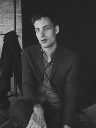 Monochrome portrait of a man in a dark suit jacket and button-down shirt seated in a studio setting