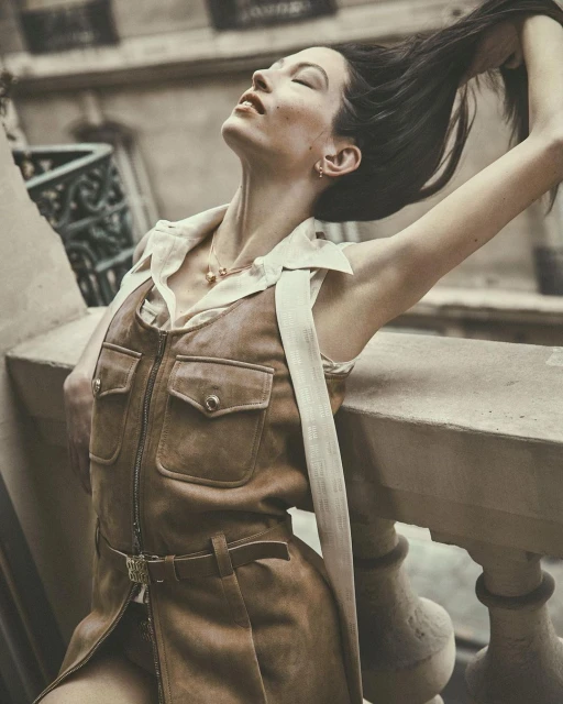 Stylish woman with long hair poses in a brown dress and white top on a balcony, bathed in soft light, creating a serene and elegant moment.