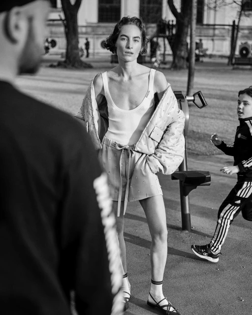 An adult woman in athleisure stands in a park with fitness equipment with two people in the background in a black and white photo.