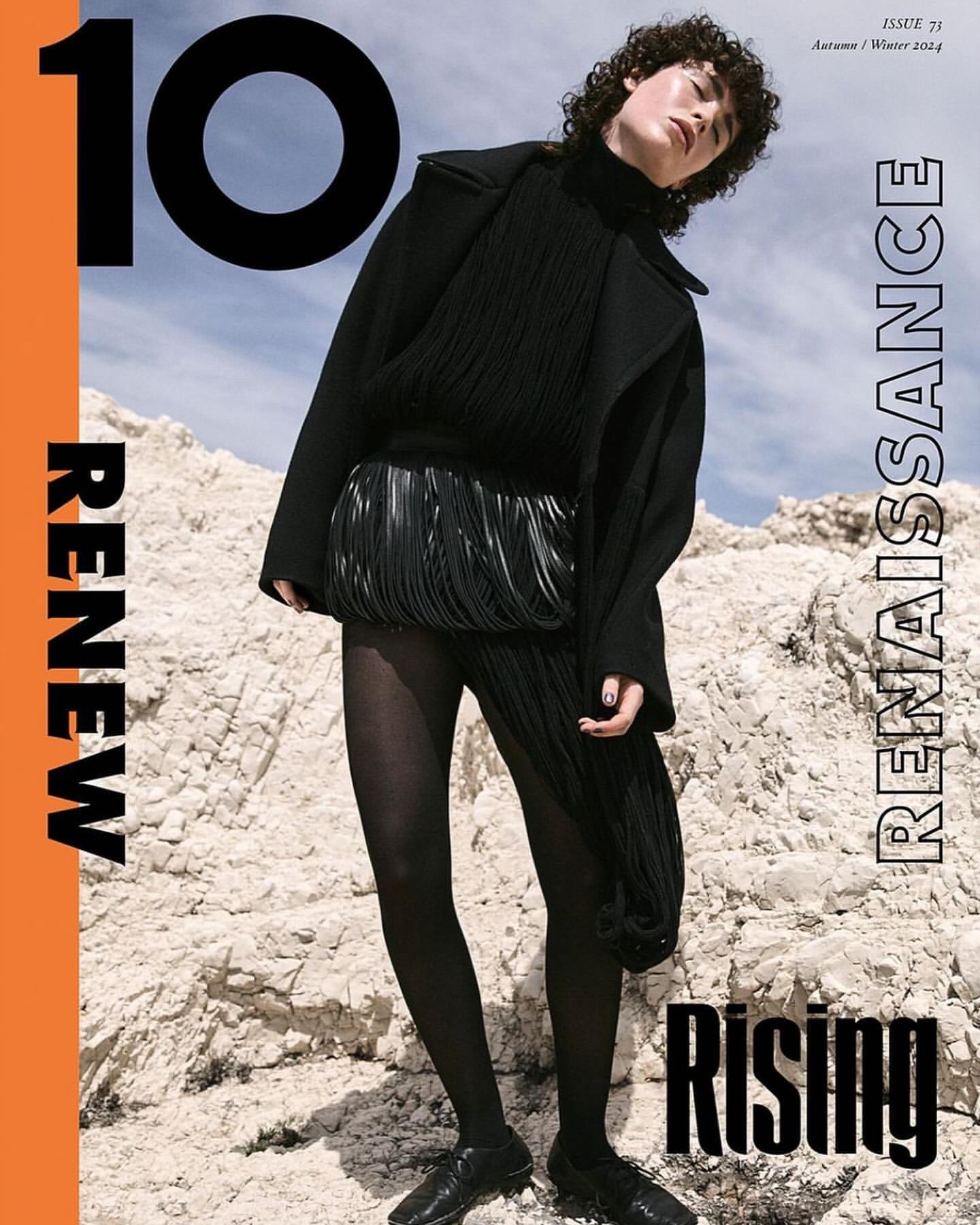 Editorial fashion shoot: Woman in black coat with fringe skirt posing on rocky terrain for a magazine cover, Autumn/Winter 2019.