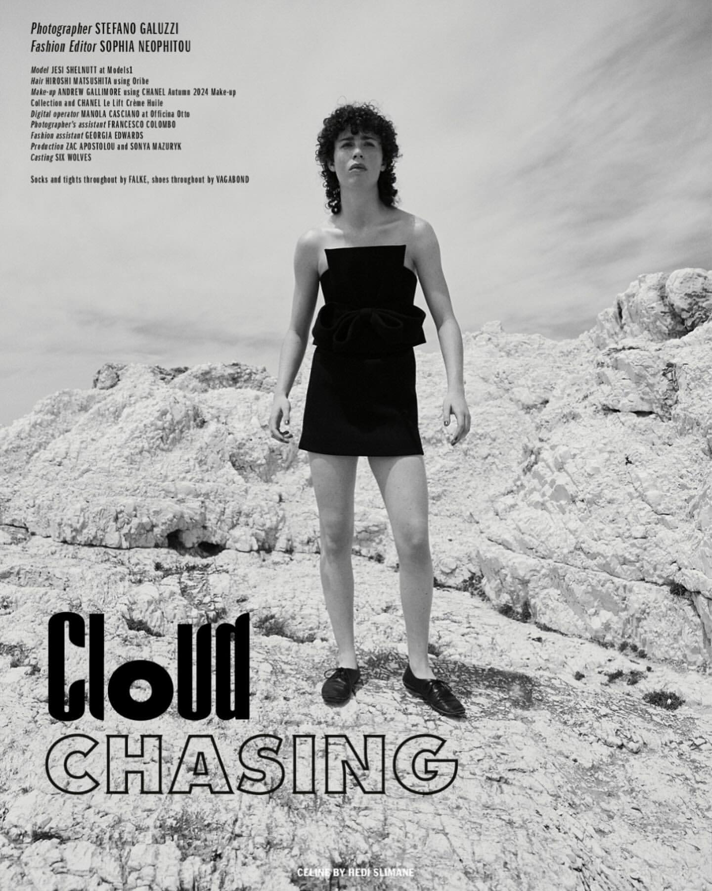 Fashion editorial photo of a person in a black dress posing on a rocky landscape under a cloudy sky. Black and white photography.