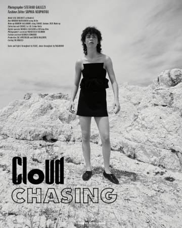 Fashion editorial photo of a person in a black dress posing on a rocky landscape under a cloudy sky. Black and white photography.
