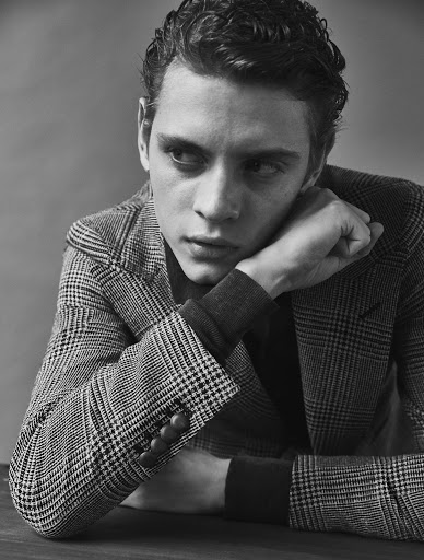 Monochrome portrait of a young man in a houndstooth blazer resting his chin on his hand, looking away.