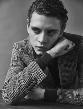 Monochrome portrait of a young man in a houndstooth blazer resting his chin on his hand, looking away.