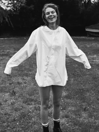 Monochrome portrait of a smiling woman in an oversized white shirt outdoors on a lawn, photographed by Stefano Galuzzi.