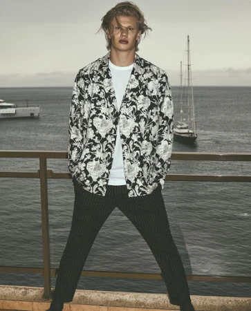 A pensive adult woman with medium-length hair and a blazer poses inside an interior space with minimalist design.