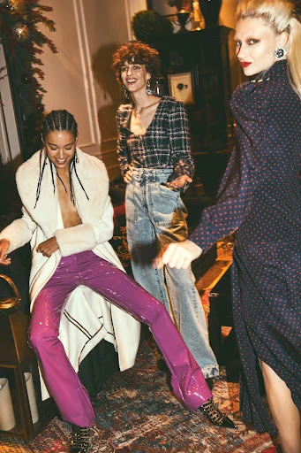 Three fashion models in an indoor setting. One model wears purple pants, one wears jeans, and the third wears a long dress.